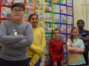  students standing in front of the handmade diversity quilt